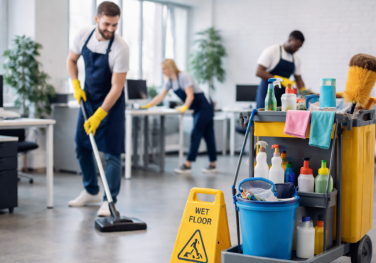 Professional janitorial services team cleaning modern office with vacuuming, disinfecting desks, and organized cleaning equipment
